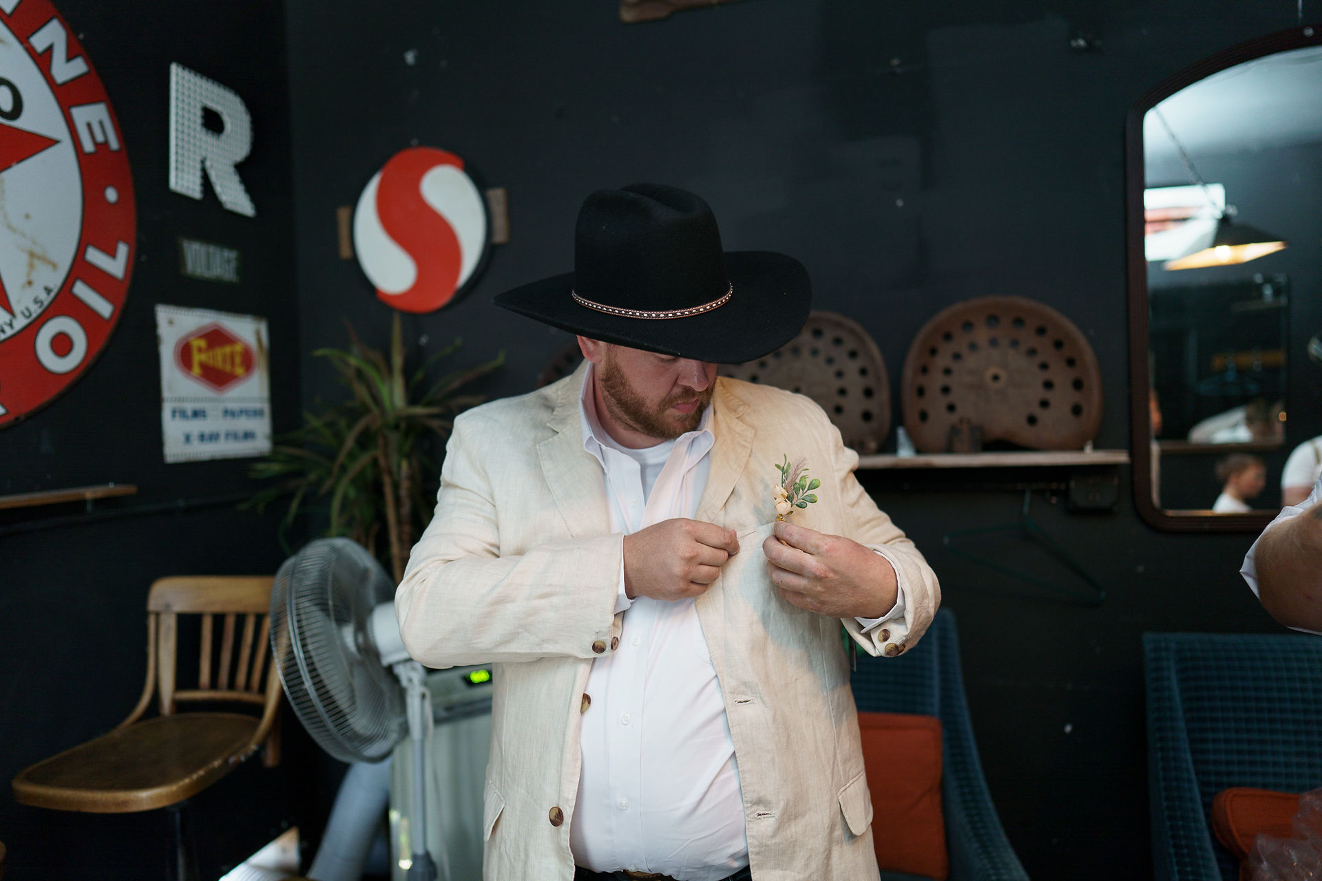 Man in black hat adjusting boutonnière on his light jacket.