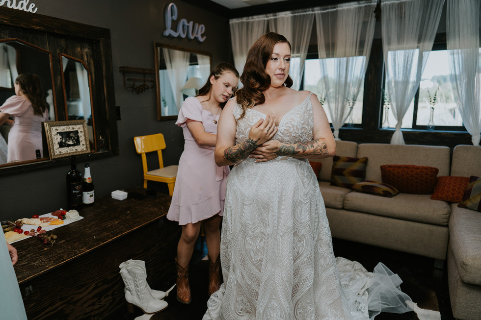 Bride getting dressed in wedding gown, bridesmaid helping, "Love" sign.