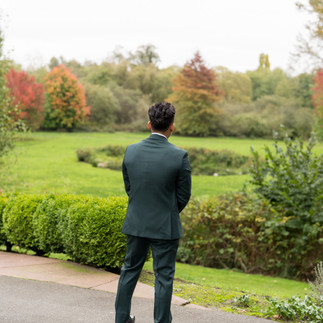 Man in dark suit stands looking at autumn garden at Sanders Estate.