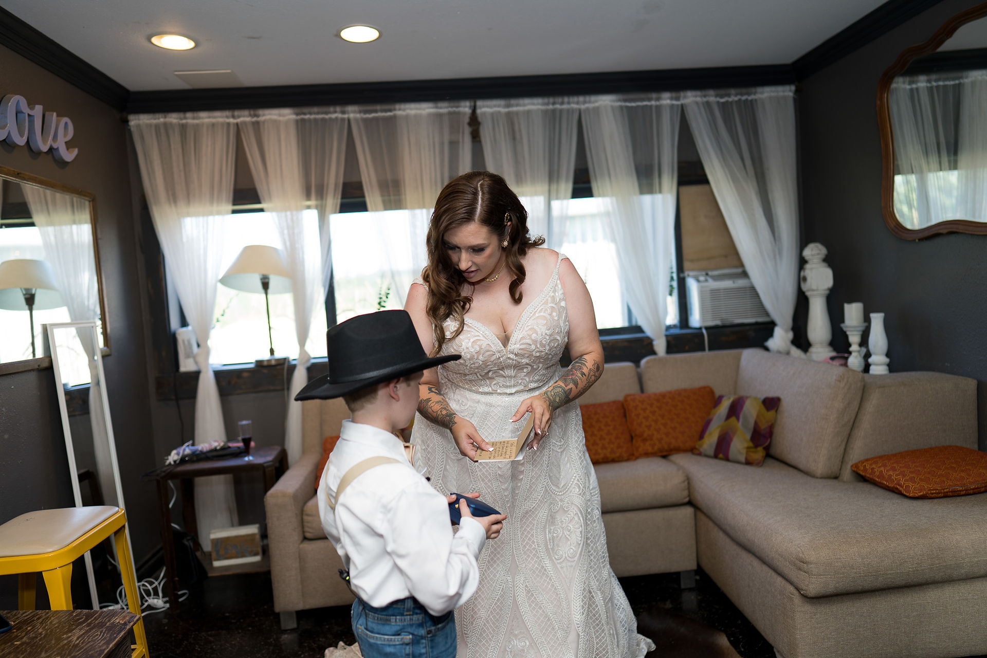 Bride in white gown looks at young boy holding box.