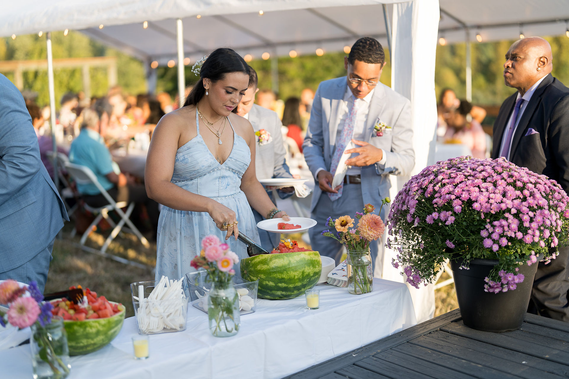 Woman serves watermelon at an outdoor wedding food table.