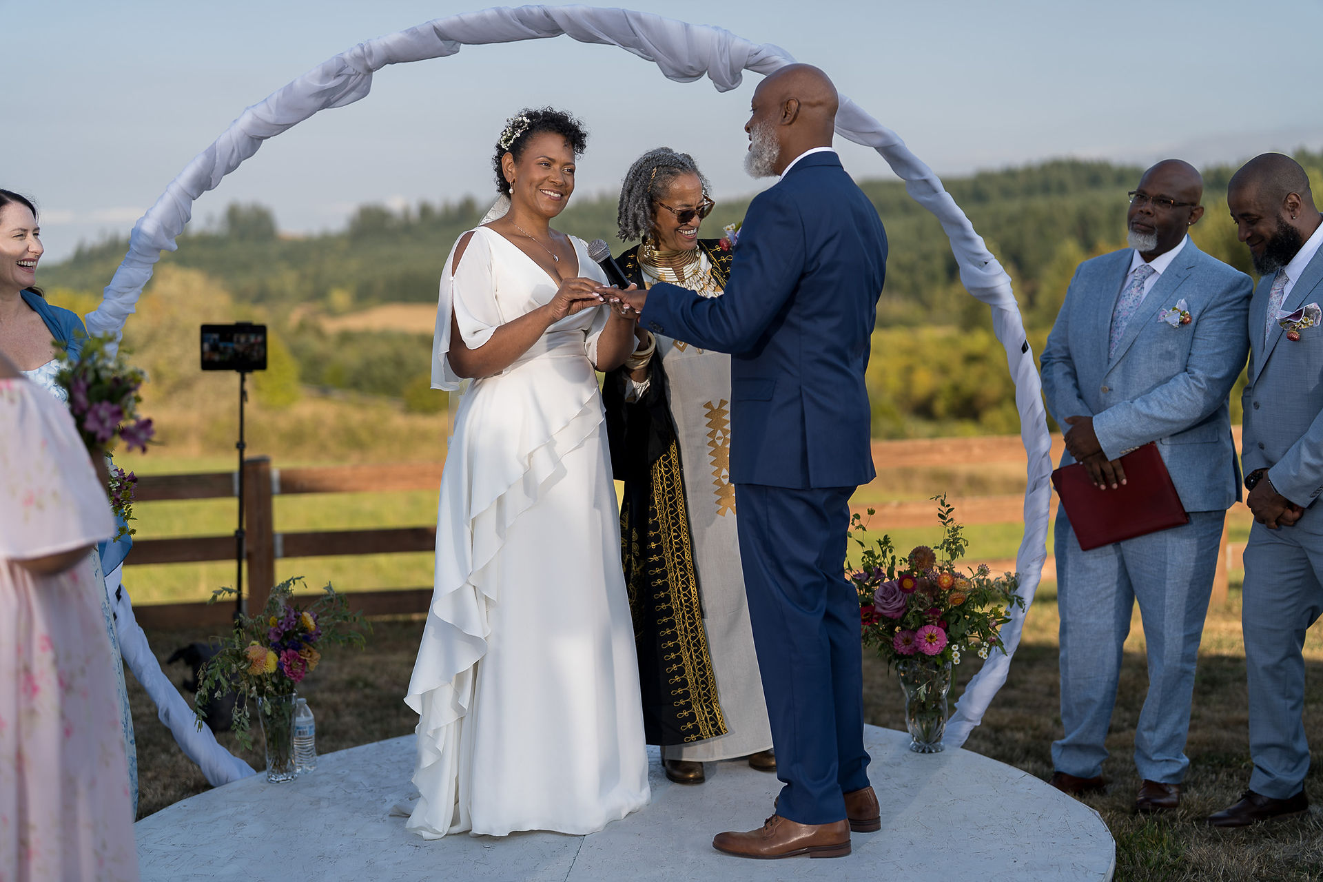 Bride and groom exchange rings at intimate farm wedding ceremony with officiant.