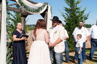 Bride and groom exchanging vows under an arch at outdoor wedding.