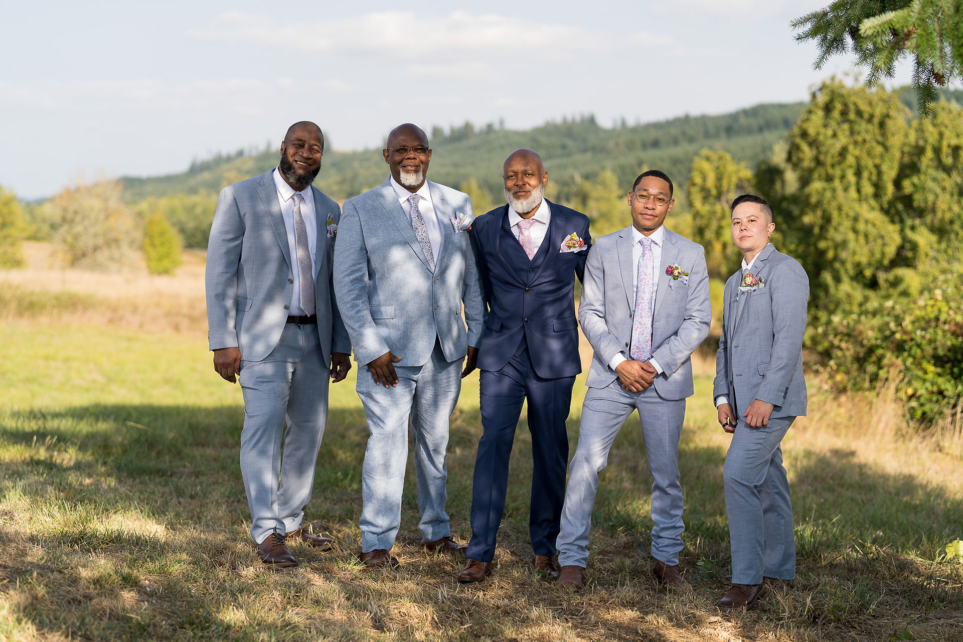 Five men in light blue and navy suits at outdoor wedding.