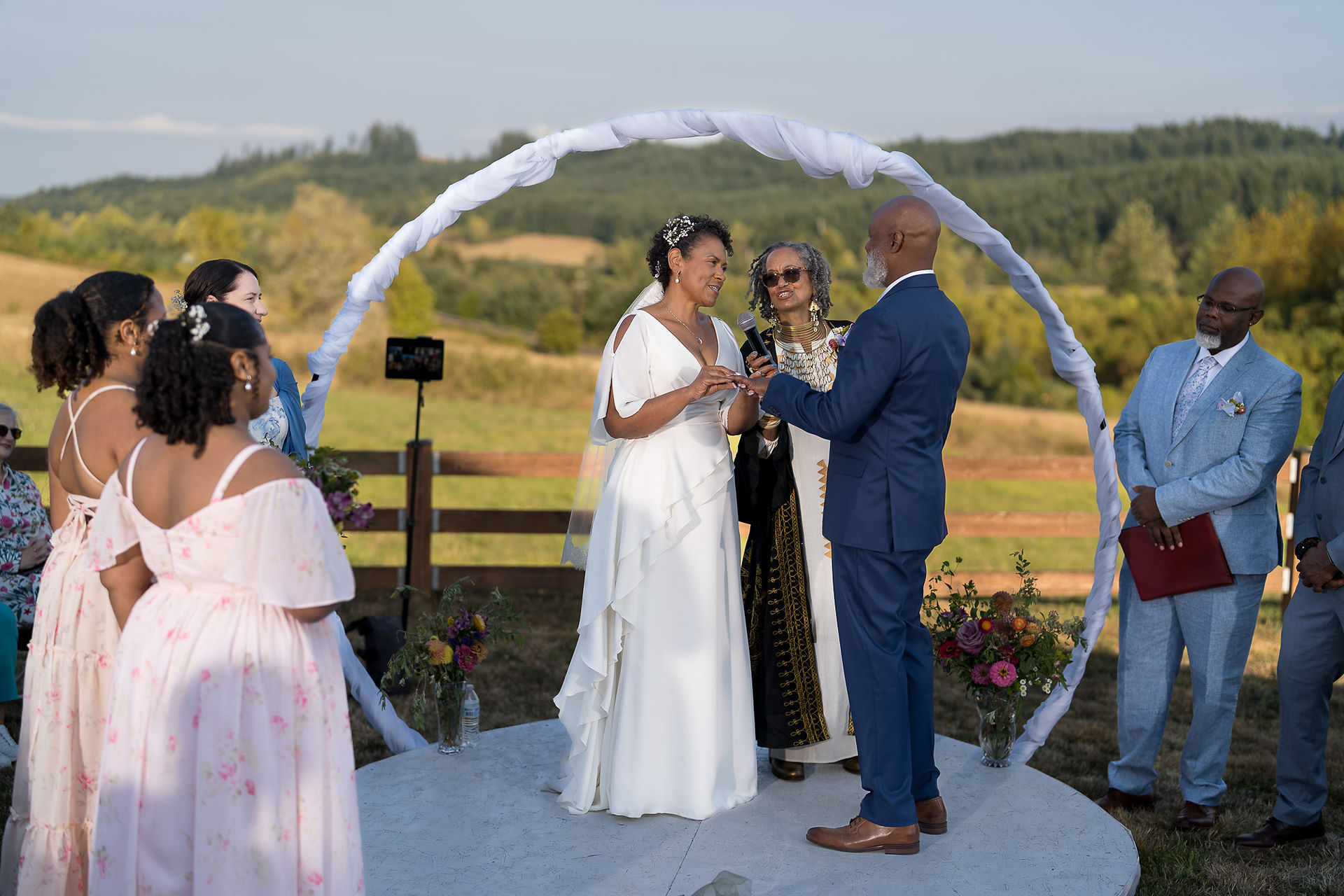 African American couple exchanging vows under a white circular arch.