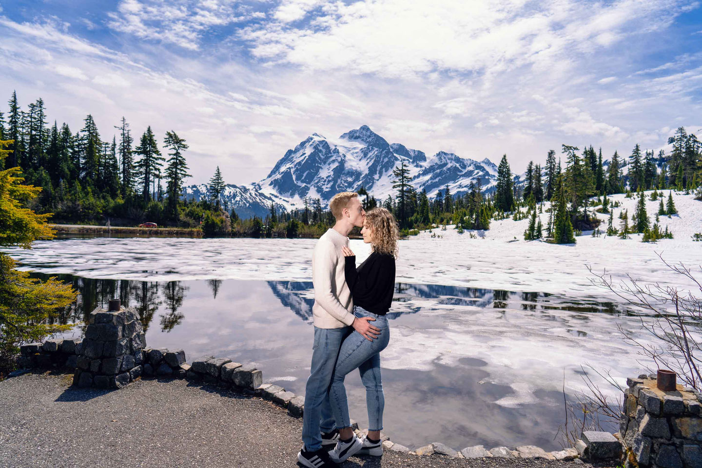 Couple embracing by frozen lake, snowy mountain. Seattle engagement photographer.