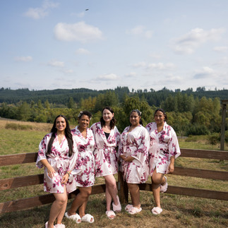Five women in floral robes and slippers by farm fence.