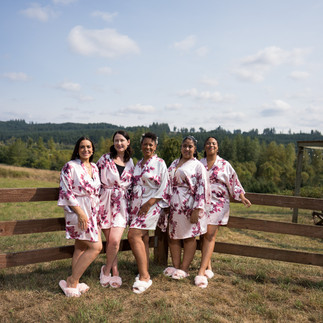 Five women in floral robes and slippers by a rustic farm fence.