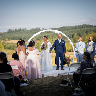 Bride and groom exchanging vows under arch at intimate farm wedding.