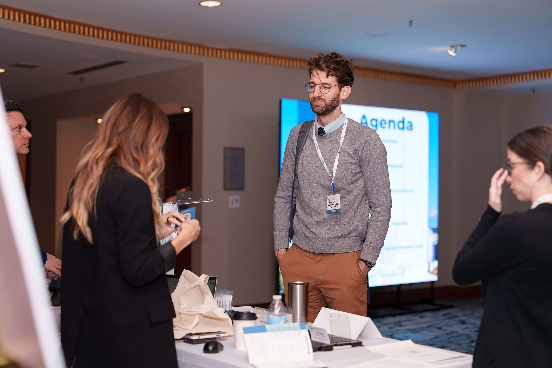 Man at IBD Pro Symposium registration desk with 'Agenda' on screen