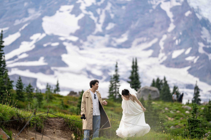 Bride and groom hiking near a majestic snowy mountain landscape.