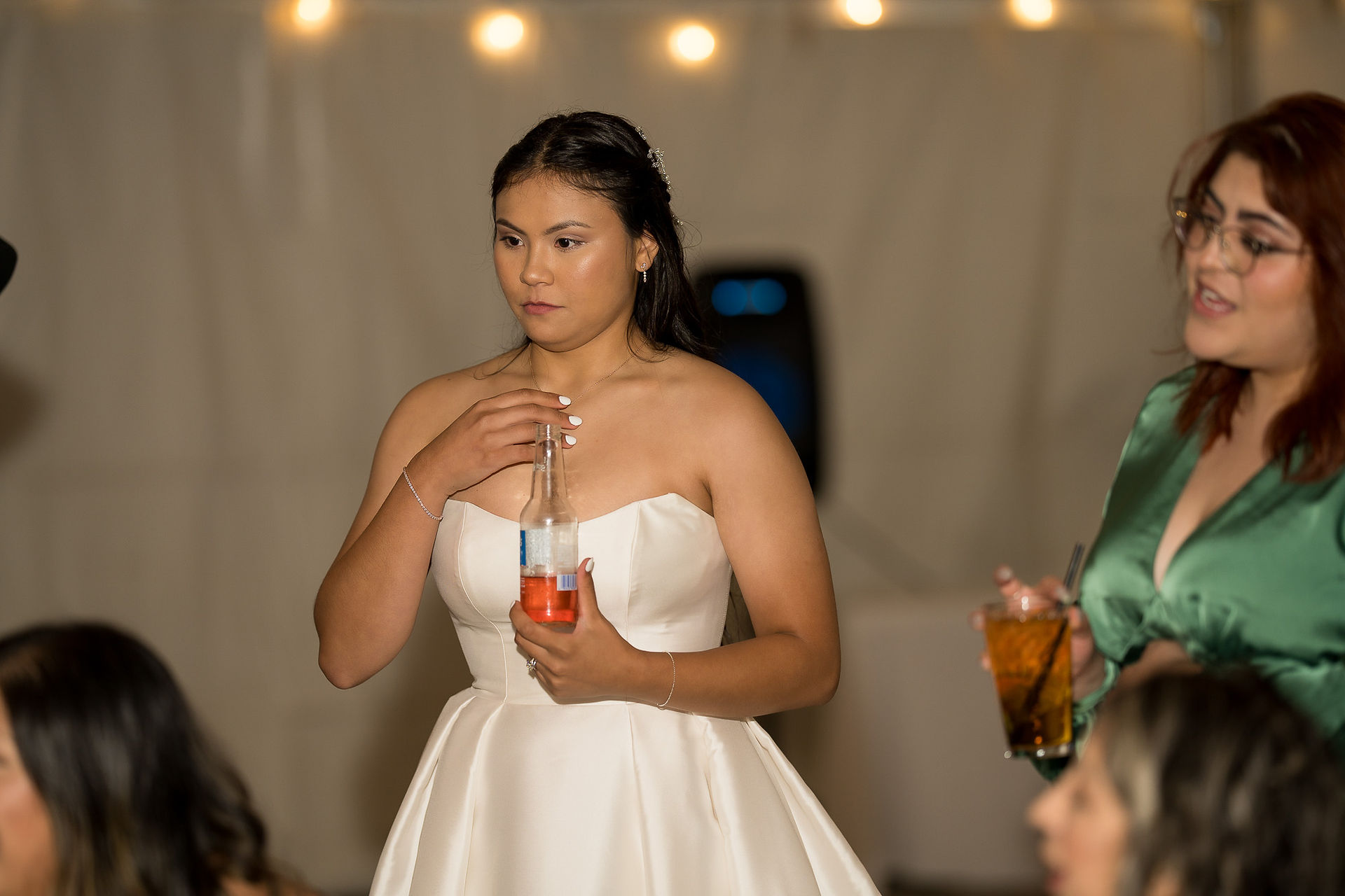 Woman in strapless wedding dress opening drink bottle at wedding reception.