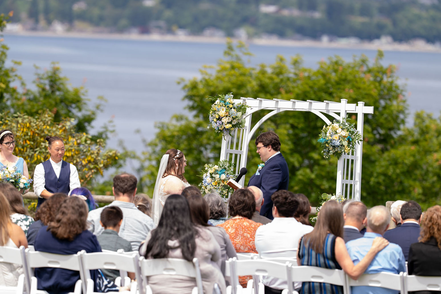 Outdoor wedding ceremony with couple, officiant, lake background, PNW photographer.