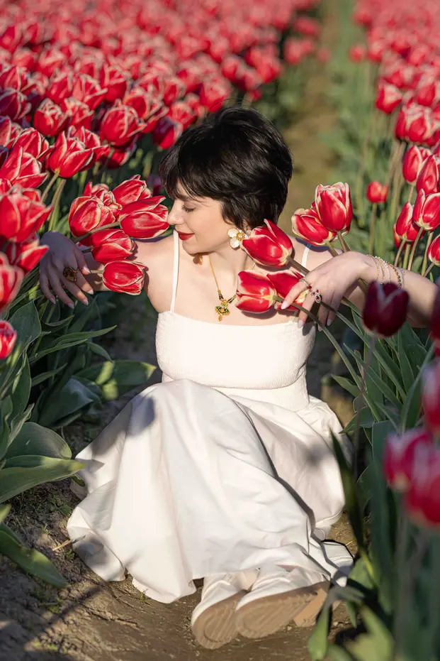 Woman in white dress sitting among red and white striped tulips.