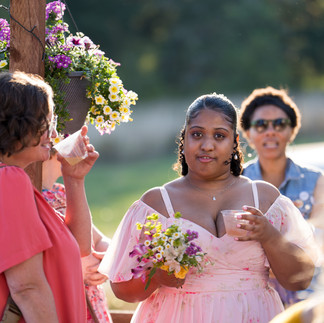 Young Black woman in pink dress holding flowers at outdoor event.