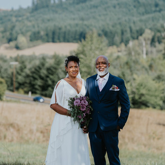 Smiling bride and groom posing outdoors with scenic rural background.