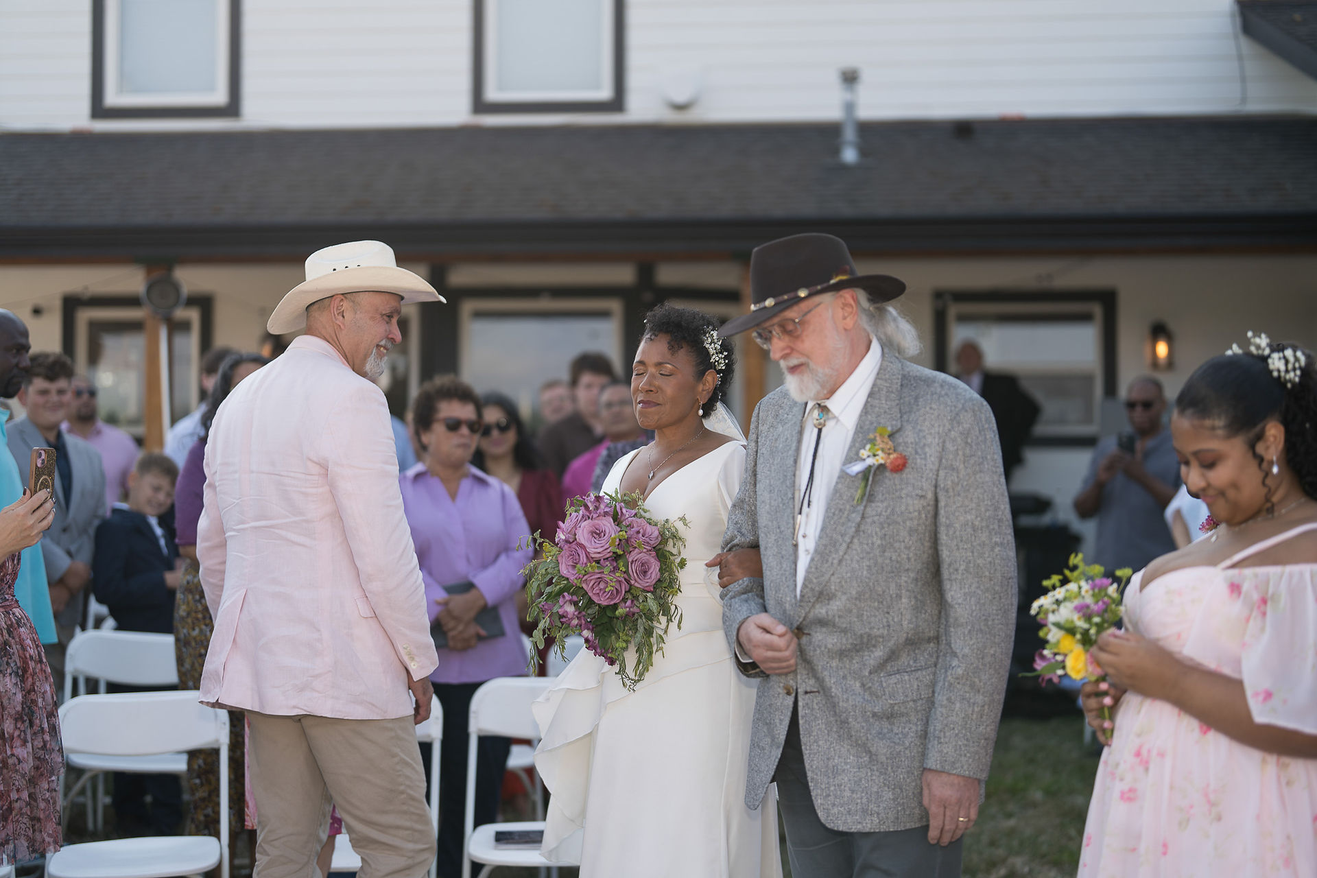 Bride walks arm-in-arm with father at intimate outdoor farm wedding.
