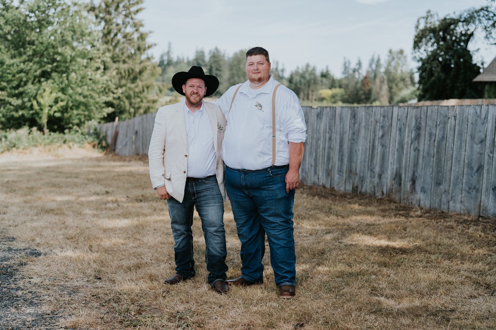 Two men, one in cowboy hat, other in suspenders, stand outdoors.