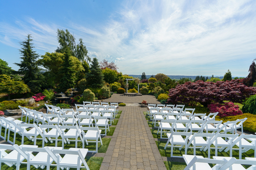 Outdoor wedding ceremony setup, white chairs, paved aisle, garden arch.