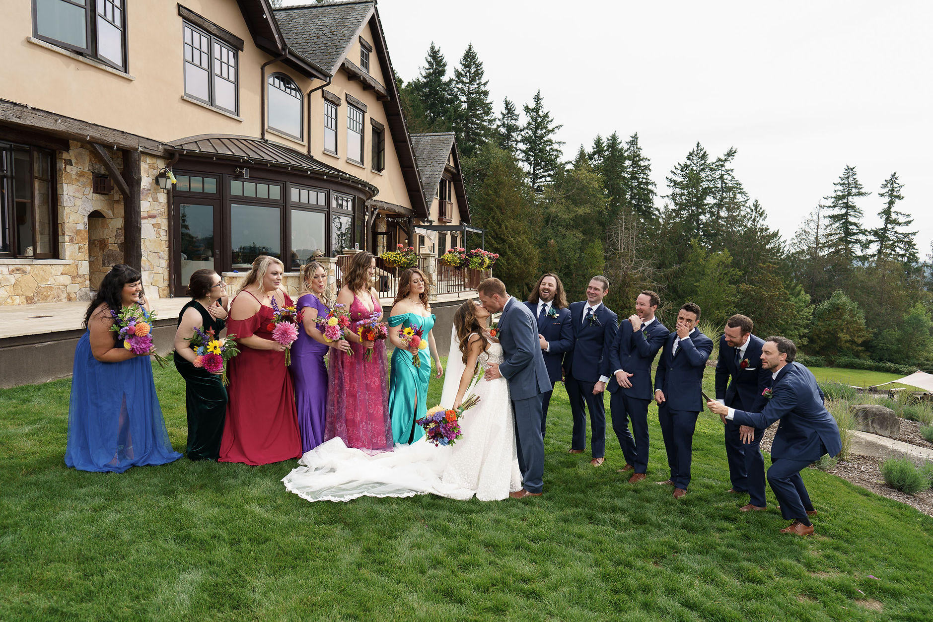 Groom kisses bride, joyful wedding party outside elegant mansion, Seattle.