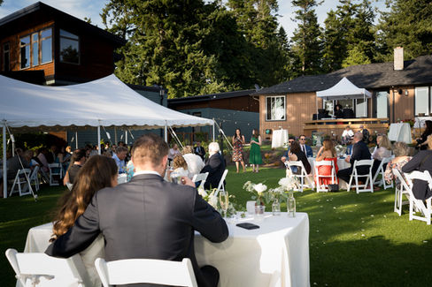 Guests enjoying an outdoor wedding reception with white tents, green lawn.