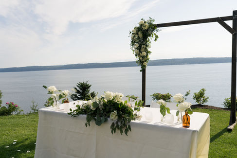Elegant outdoor wedding table with floral arch overlooking serene water.