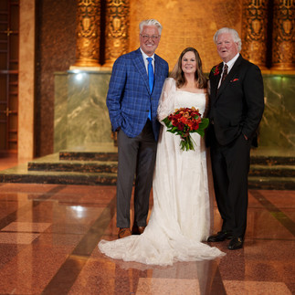 Joyful bride holding red bouquet with two men in ornate chapel.