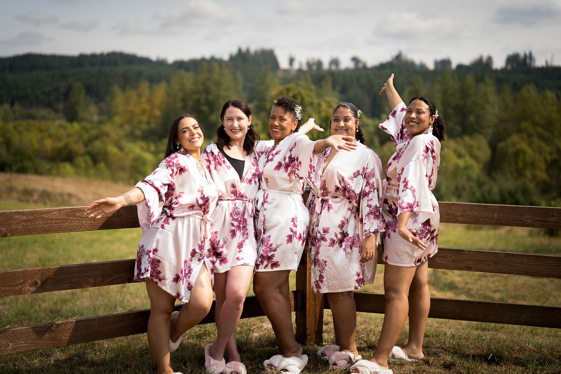 Five smiling women in floral robes posing outdoors at farm.