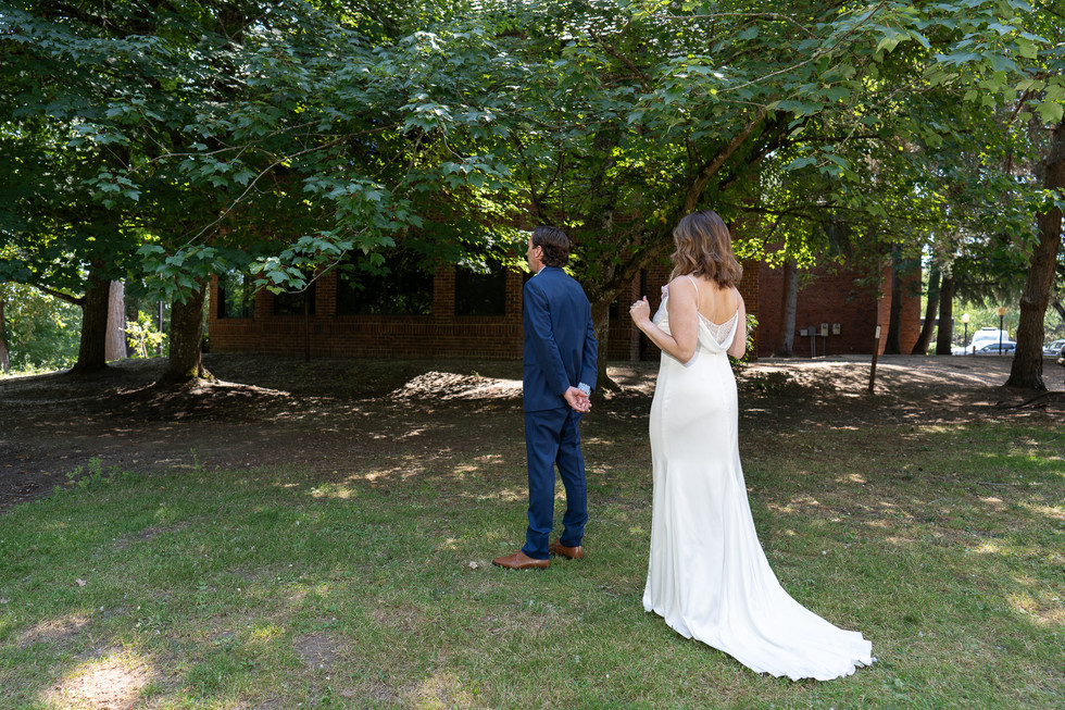 Groom in blue suit, bride in white dress, backs to camera.