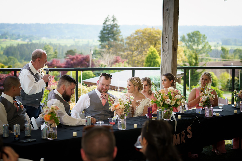 Bride and groom at outdoor wedding reception table with 'MRS' sign.