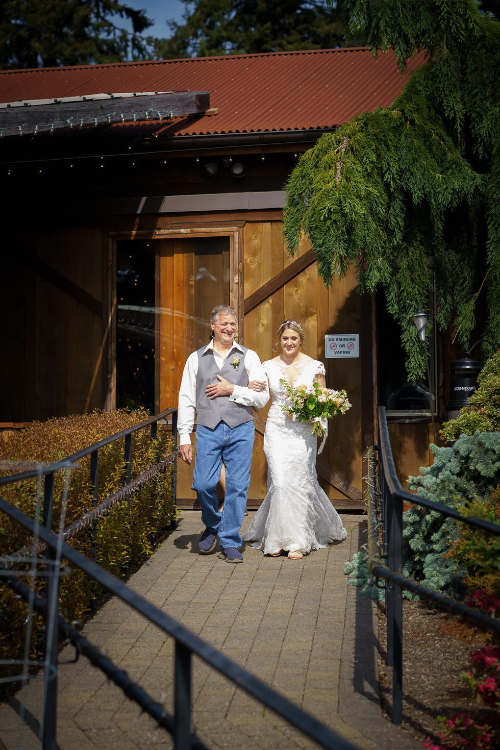 Father walks bride down outdoor path toward Olympic View Wedding Estates.
