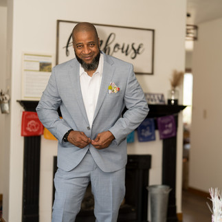 Smiling man in light blue suit adjusting jacket, Farmhouse sign background.