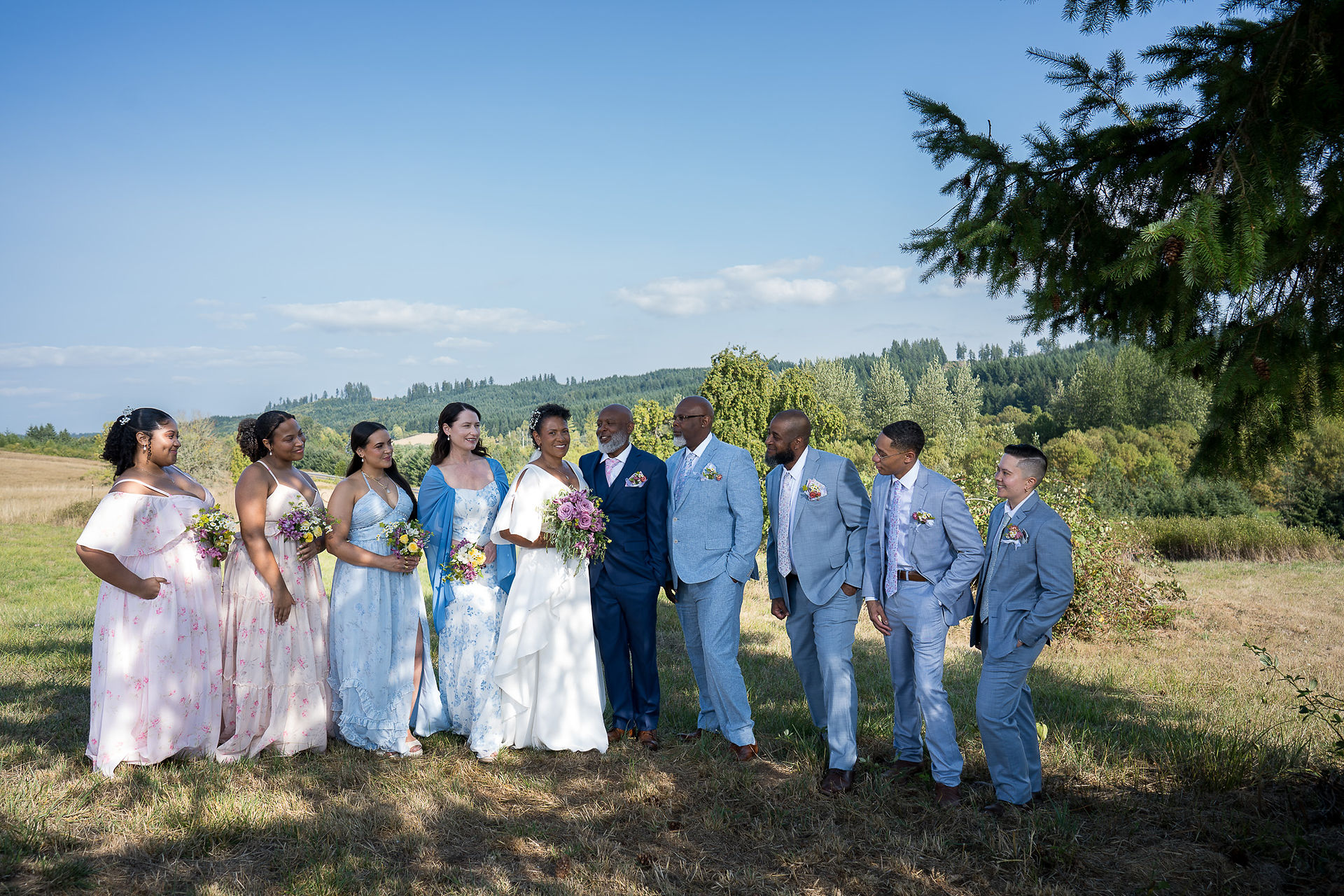 Wedding party poses outdoors in a sunny field under blue sky.