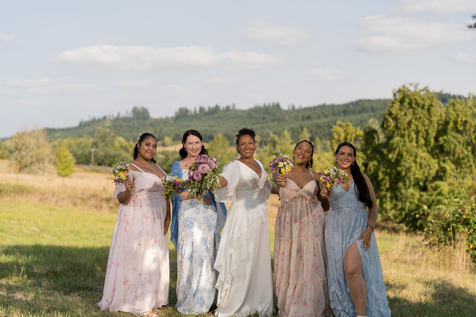 Five smiling women, bride and bridesmaids, holding bouquets at farm wedding.