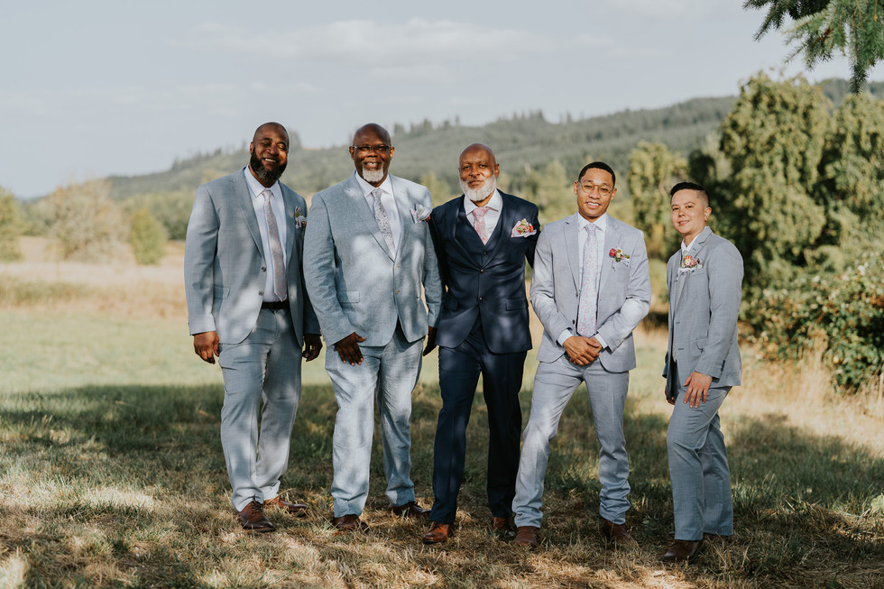 Five groomsmen in light and dark suits posing outdoors at wedding.