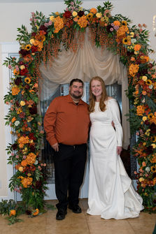 Newlyweds posing under beautiful autumn floral wedding archway.