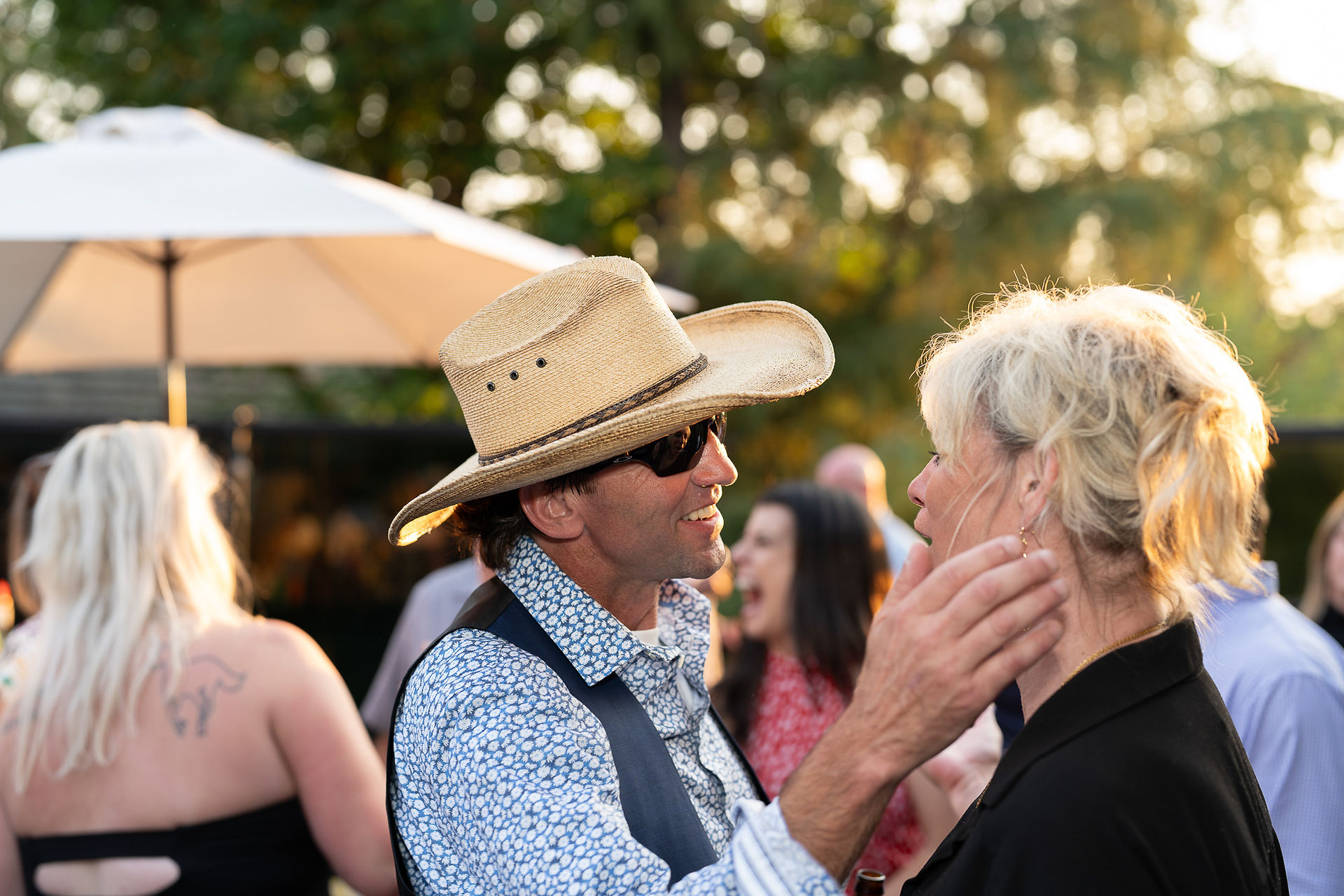 Man in straw cowboy hat, sunglasses, talking to woman outdoors.