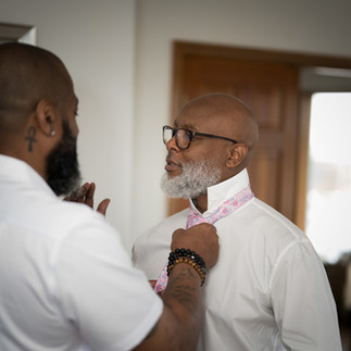 Bearded man helps older man in glasses adjust patterned pink tie.