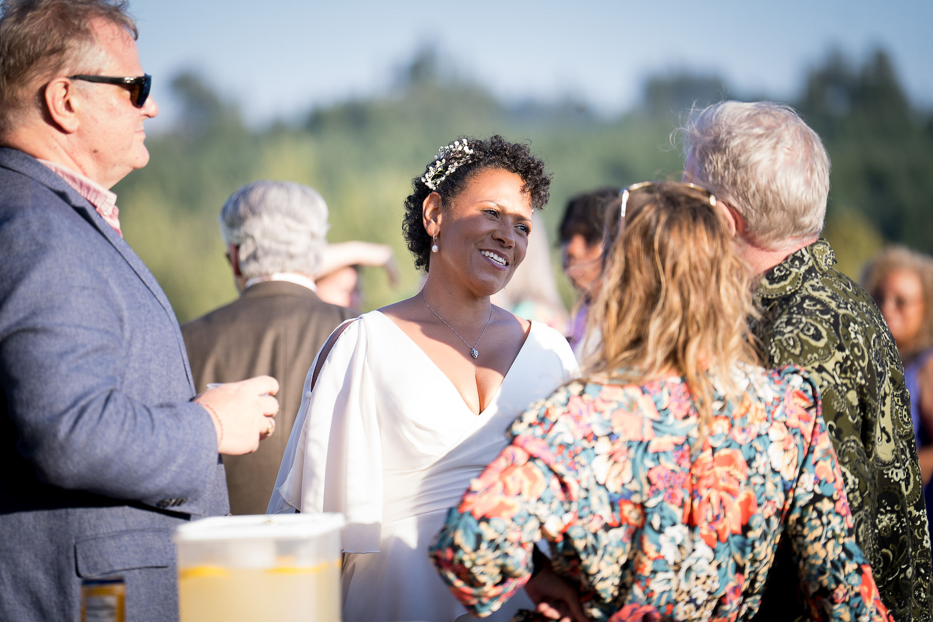 Woman in white dress smiling, talking to guests at Intimate Farm Wedding.