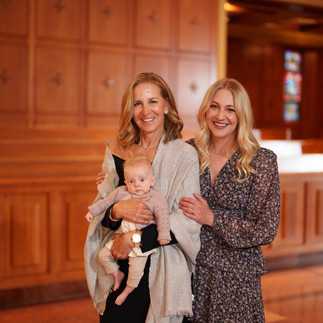 Two smiling women, one holding a baby, inside a chapel.