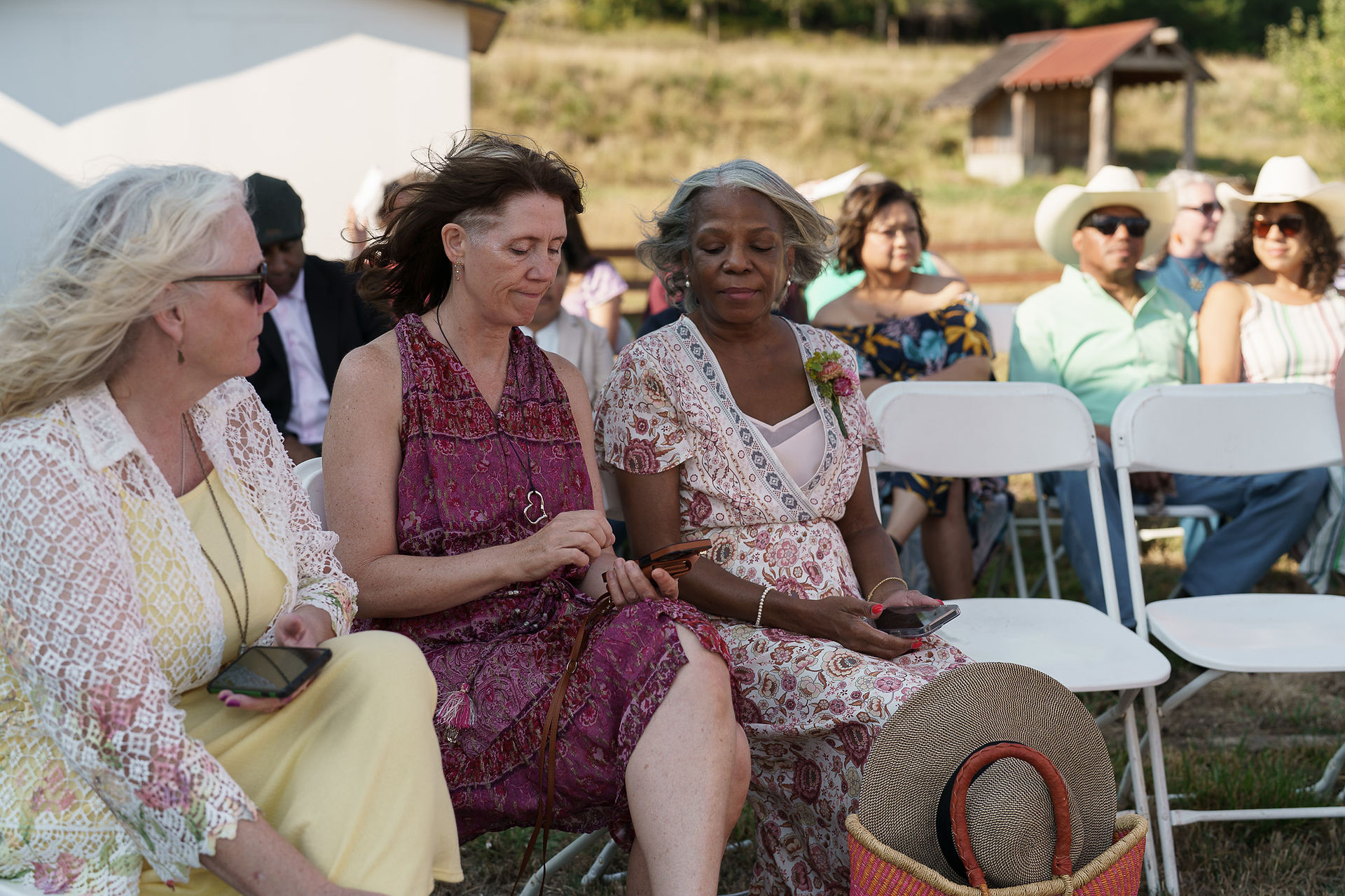 Two women, wedding guests, seated at an outdoor farm ceremony.