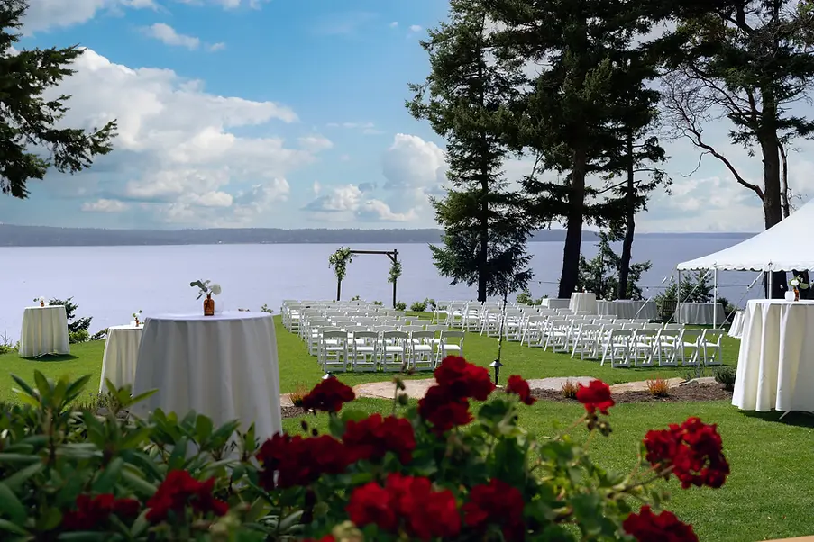 Waterfront wedding ceremony setting with white chairs and a floral arch