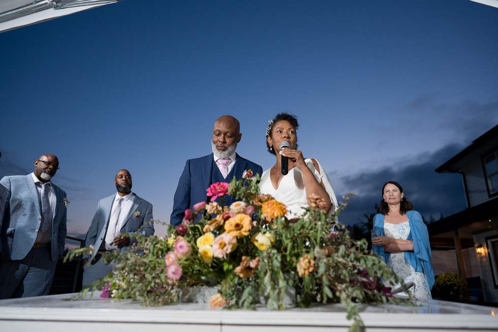 Woman speaking into microphone at outdoor wedding reception, with flowers.