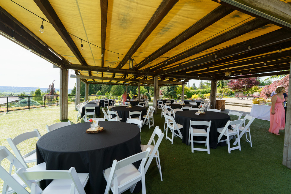 Covered outdoor reception area with black tables, white chairs, green floor.