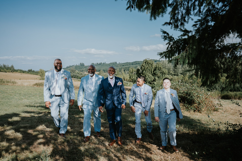 Five groomsmen in suits walking outdoors, intimate farm wedding setting.