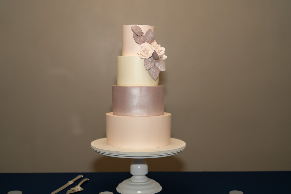 Four-tiered wedding cake decorated with delicate pink flowers and leaves.