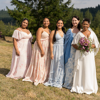 Five women smiling at an intimate farm wedding, wearing pastel dresses.