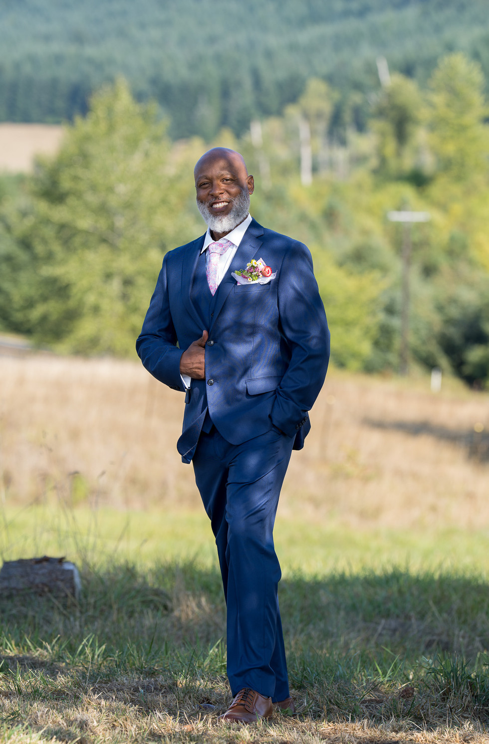 Smiling Black man in navy suit with floral pocket square outdoors.