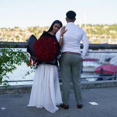 Couple embraces near waterfront, holding red roses