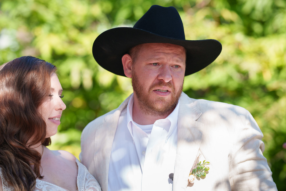 Man in black cowboy hat and light suit jacket at outdoor wedding.